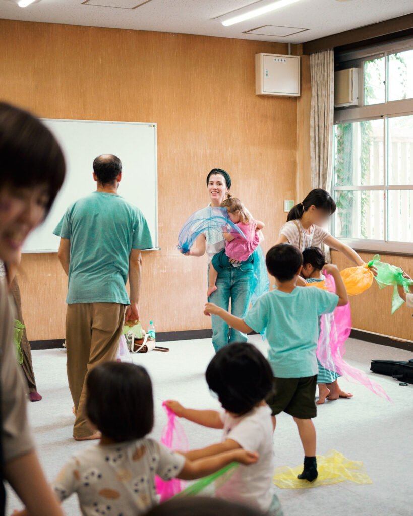 Jeweliann leading a Saturday class at the Sakyo West Area Iki-Iki Citizen Activity Center, families waving colorful scarves in a bright room